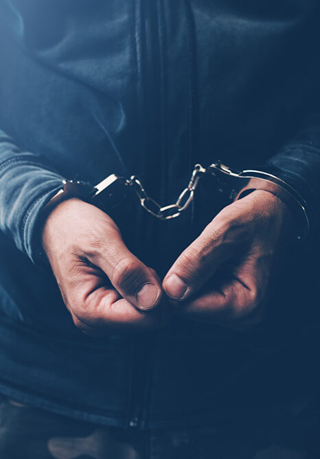 Arrested computer hacker and cyber criminal with handcuffs, close up of hands