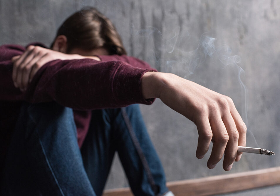 Close-up view of depressed teenage boy sitting with cigarette in hand