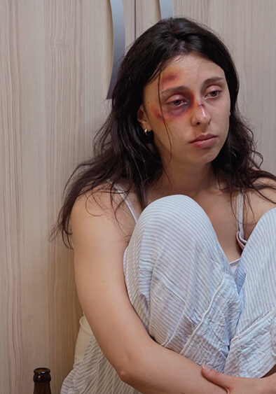 Drunk man lying on the floor near beaten wife. Traumatised abused terrified vulnerable woman covered in bruises suffering injury from violent alcoholoic brutal man.