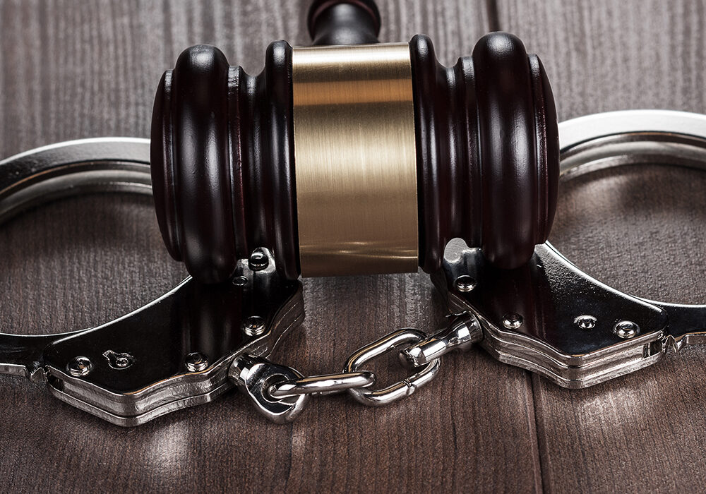 handcuffs and judge gavel on brown wooden table background