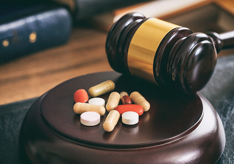 Law gavel and colorful pills on a wooden desk, dark background
